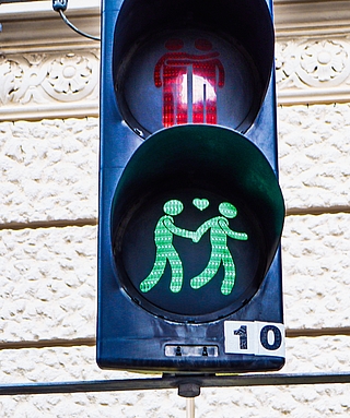 Diese Fußgängerampel in Wien zeigt oben zwei Männer, die sich bei Rot umarmen, und unten zwei Männer, die bei Grün Hand in Hand gehen. Zwischen ihnen schwebt ein leuchtendes Herz. (Foto: Björn Hildebrand)