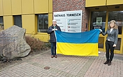 Bürgervorsteher Friedrich Meyer-Hildebrand und Bürgermeisterin Sabine Kählert breiteten vor dem Rathauseingang die ukrainische Flagge aus. Diese wurde anschließend vor dem Verwaltungssitz gehisst. (Foto: Stadt Tornesch)