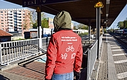 Am Elmshorner Bahnhof steht ein Reisendenhelfer auf dem Bahnsteig zwischen den Gleisen 2 und 3. Er bietet Fahrgästen mit schweren Koffern, Kinderwagen und E-Bikes seine Hilfe an. Im Hintergrund sind die Bretterwände zu sehen, mit denen der Fahrstuhlschacht abgesperrt ist – voraussichtlich noch bis Anfang September. (Foto: Frank)