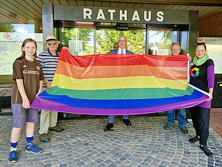 Zeigen Flagge vor dem Uetersener Rathaus anlässlich des IDAHOBIT 2024: Mathilda Stange (von links), Rudolf Engels, Dirk Woschei, Jens Ewald und Katrin Stange. (Foto: Anna Winterberg, Stadt Uetersen)