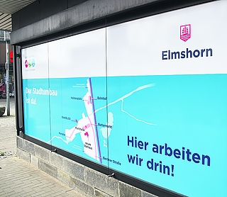 Das Schaufenster auf der Krückau-Seite ist beklebt. Die Aufschrift „Hier arbeiten wir drin!“ soll sicherlich humorvoll klingen. Stimmen würde aktuell aber die weniger witzige Formulierung „Hier arbeiten wir dran!“. (Foto: Frank)