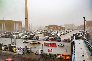 Der Schornstein steht neben dem Rewe-Markt. Fast die Hälfte der Parkplätze auf dem Supermarktdach und einige Stellflächen vor dem Gebäude werden für zwei Monate gesperrt. (Foto: Frank)