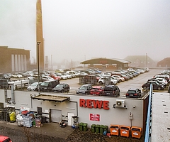 Der Schornstein steht neben dem Rewe-Markt. Fast die Hälfte der Parkplätze auf dem Supermarktdach und einige Stellflächen vor dem Gebäude werden für zwei Monate gesperrt. (Foto: Frank)