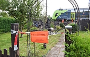 Die Polizei hat den Brandort in der Kleingartenanlage Fuchsberg in Elmshorn abgesperrt. Ein Regionalzug fährt im Schritttempo daran vorbei. Mitarbeiter der Deutschen Bahn untersuchen die technischen Anlagen. (Foto: Frank)
