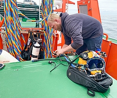 Berufstaucher Tjark Lange aus Krempe bereitet auf dem Vermessungsboot seinen Helm vor für die Wrackuntersuchung vor. (Foto: Joker Pictures)