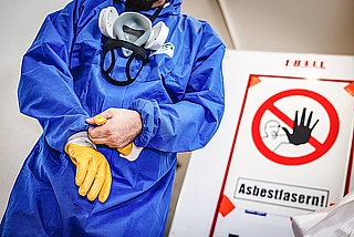 So läuft Asbest-Sanierung: Overall, Atemschutzmaske, Handschuhe und dazu noch eine Schutzbrille. „Komplett-Schutz ist ein Muss“, sagt die Bau-Gewerkschaft. (Foto: IG BAU | Alireza Khalili)